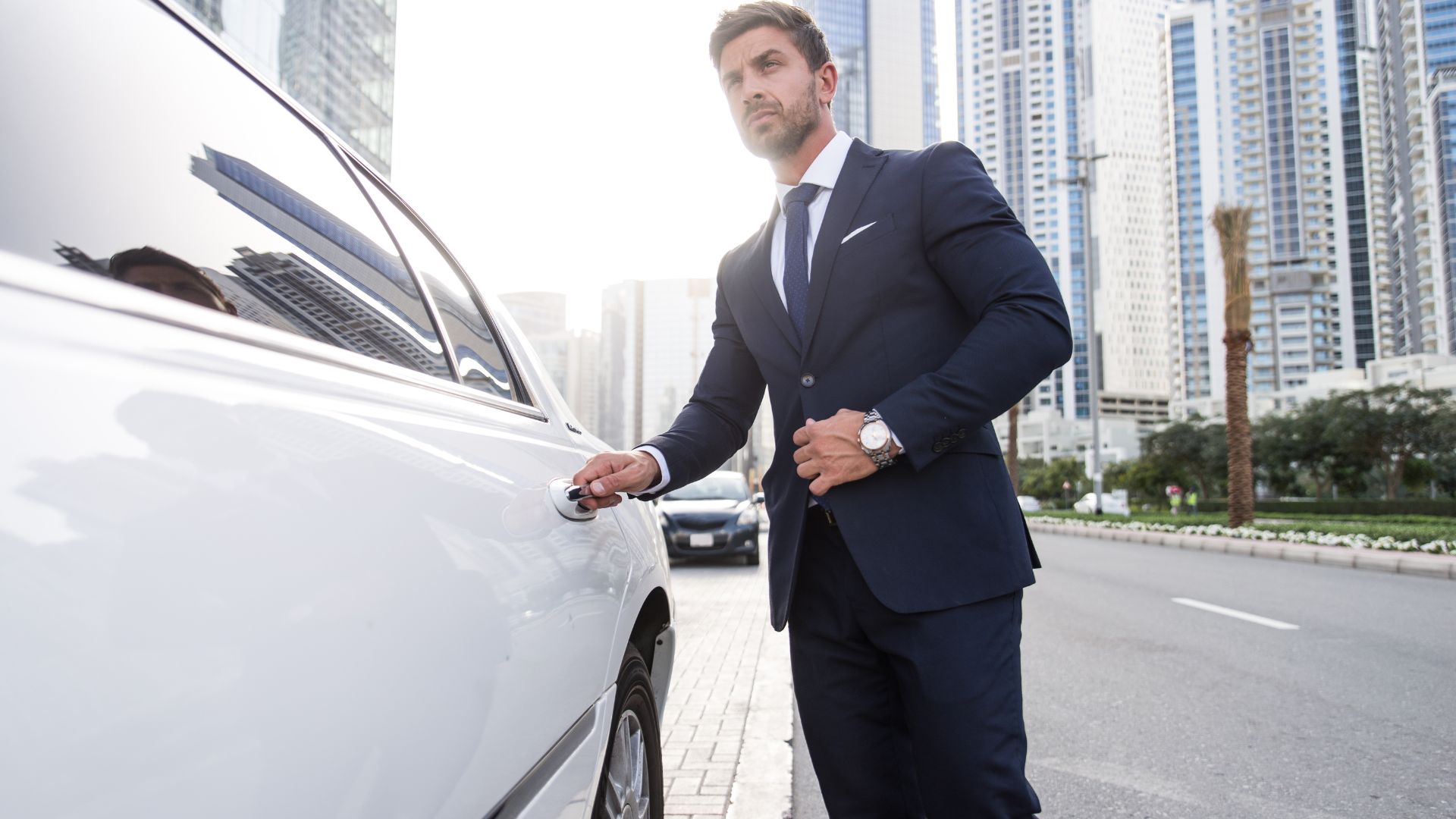 Man in suit opening car door in city.