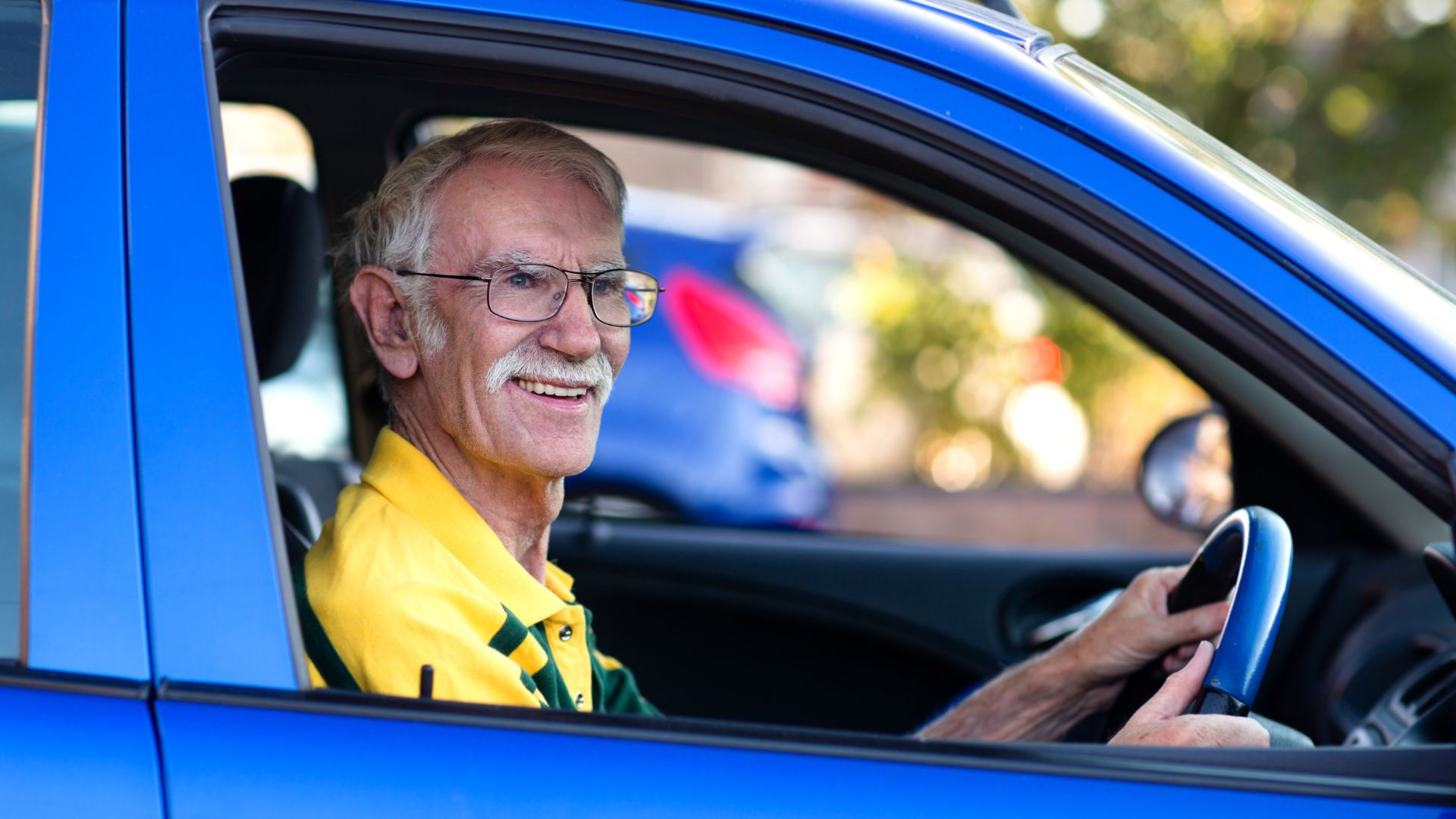 Senior man smiling while driving a blue car.