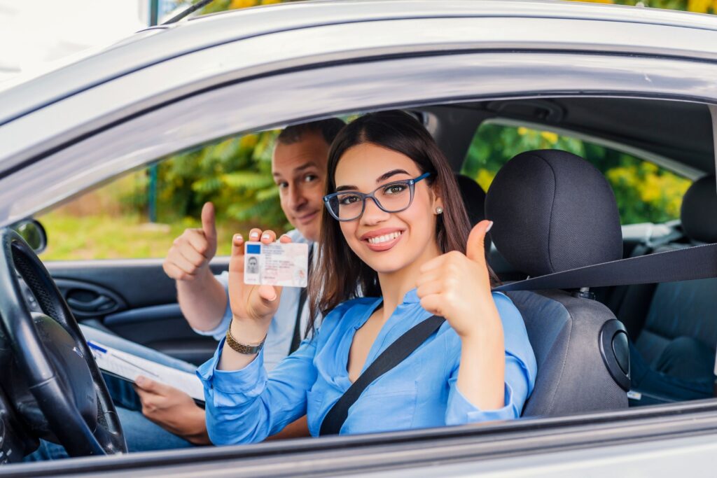 Young woman showing new drivers license in car, thumbs up.