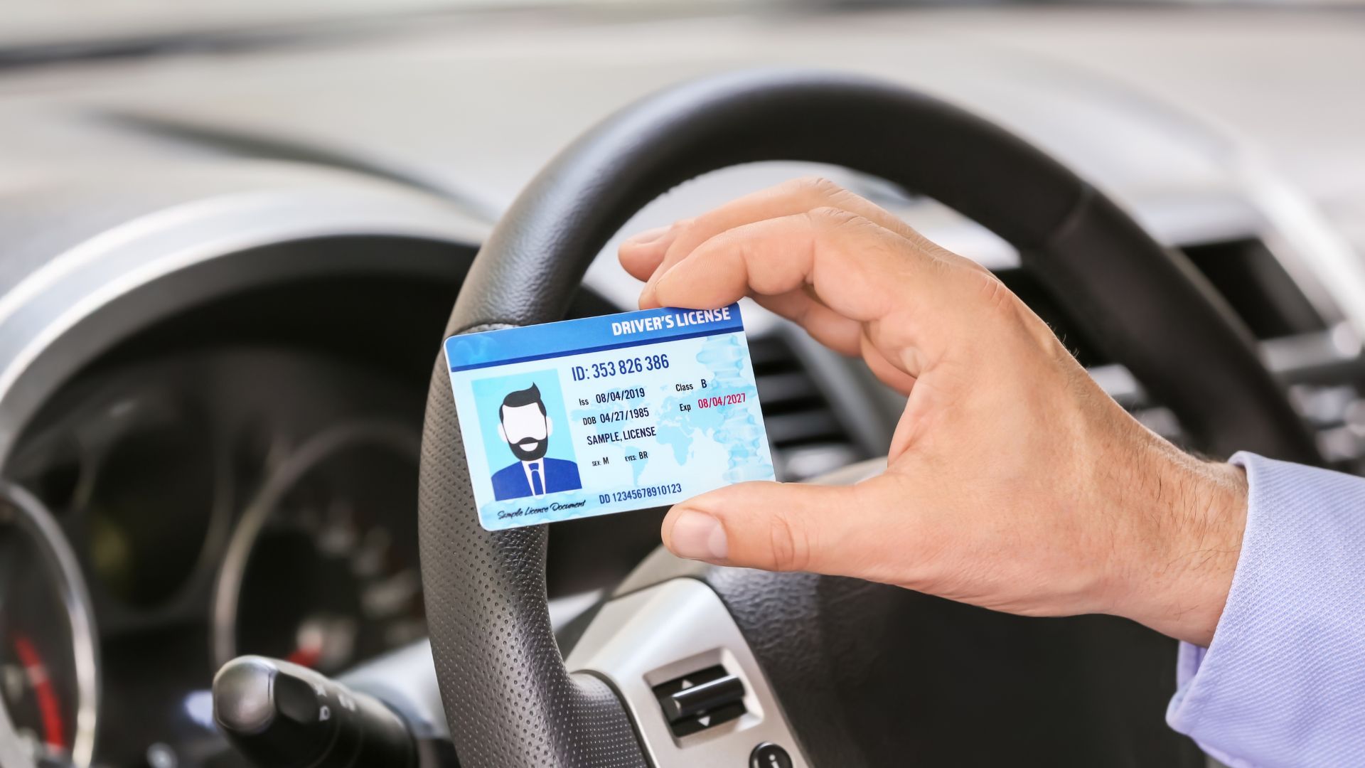 Man holding drivers license inside a car.