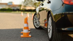 Car driving through orange traffic cones on road.