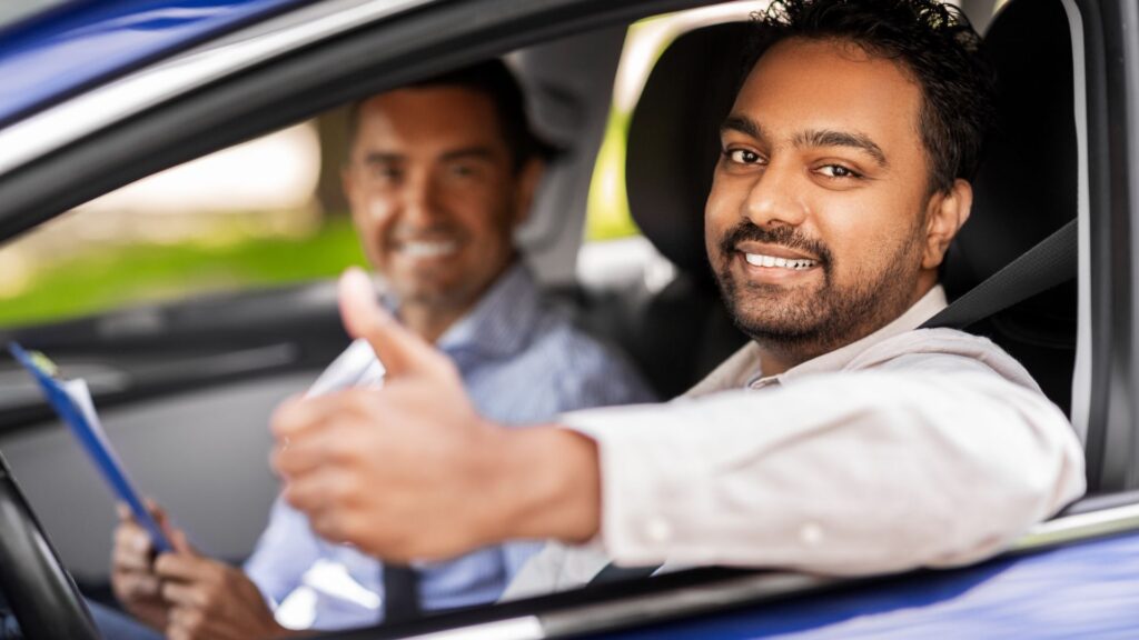 Two men smiling in car, one giving thumbs up.