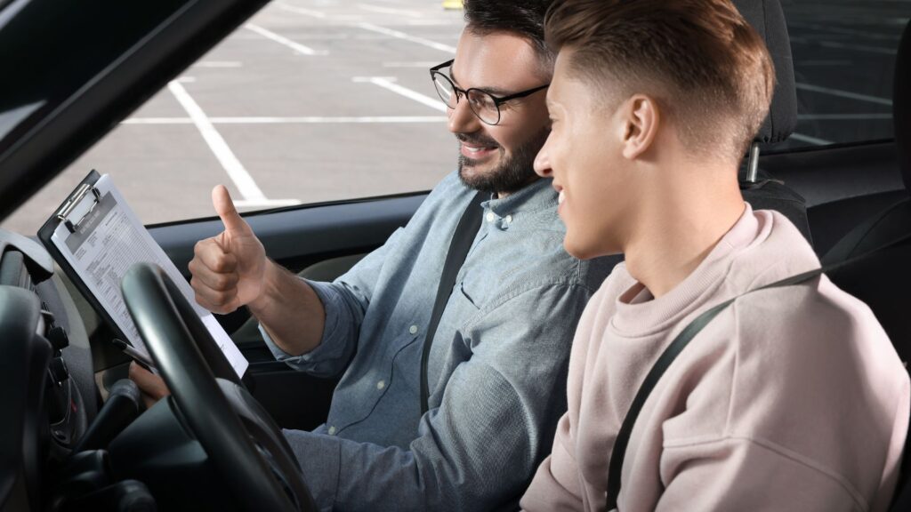 Driving instructor giving thumbs-up to male student in car.