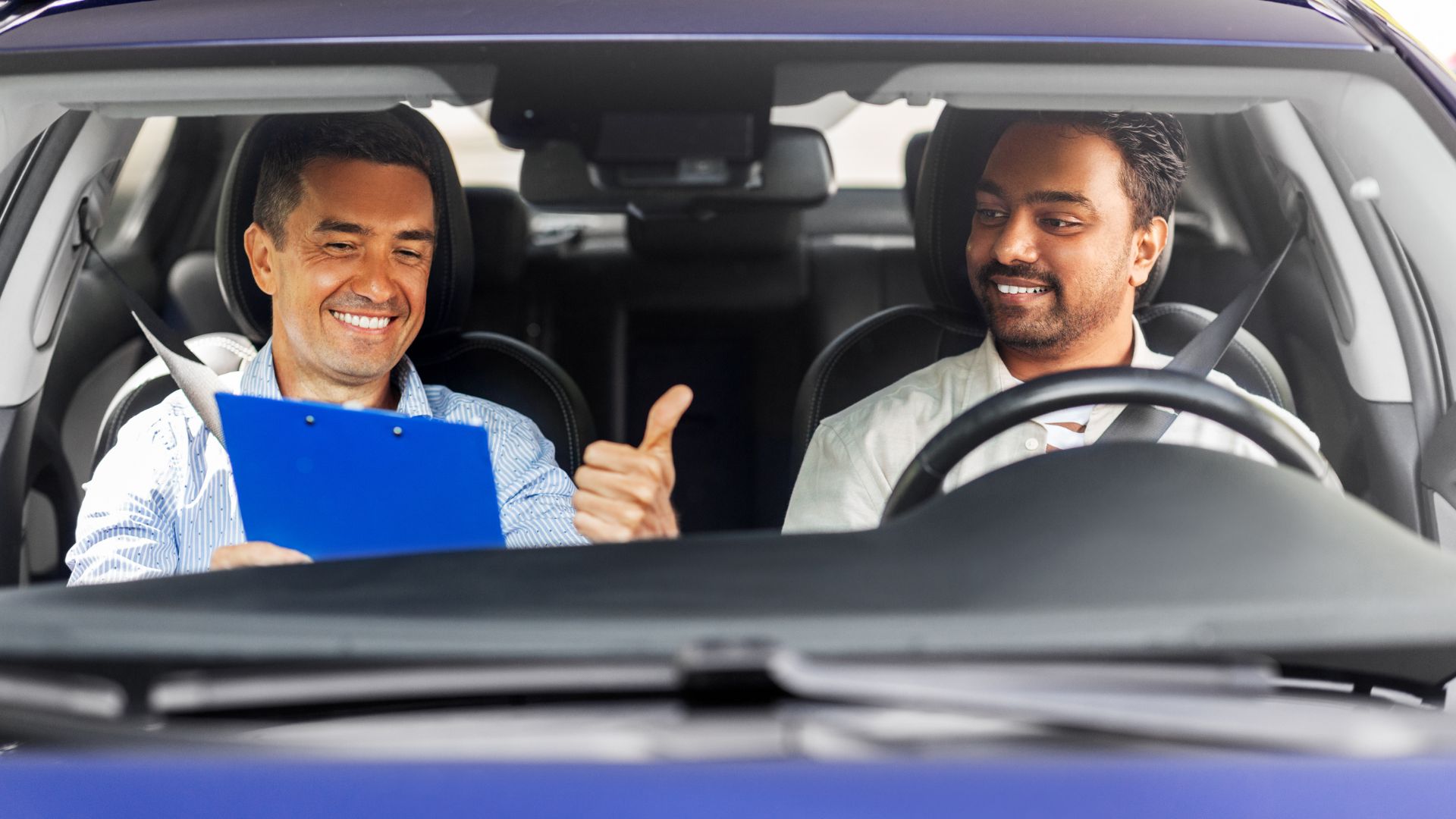 Driving instructor giving thumbs up to student in car.