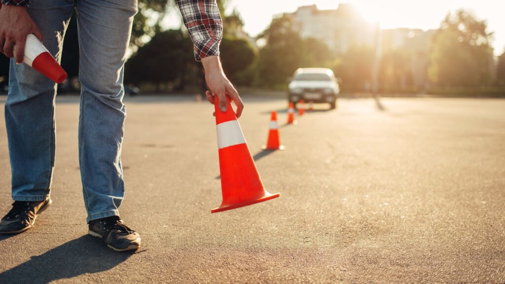 Person setting traffic cones on sunlit street.