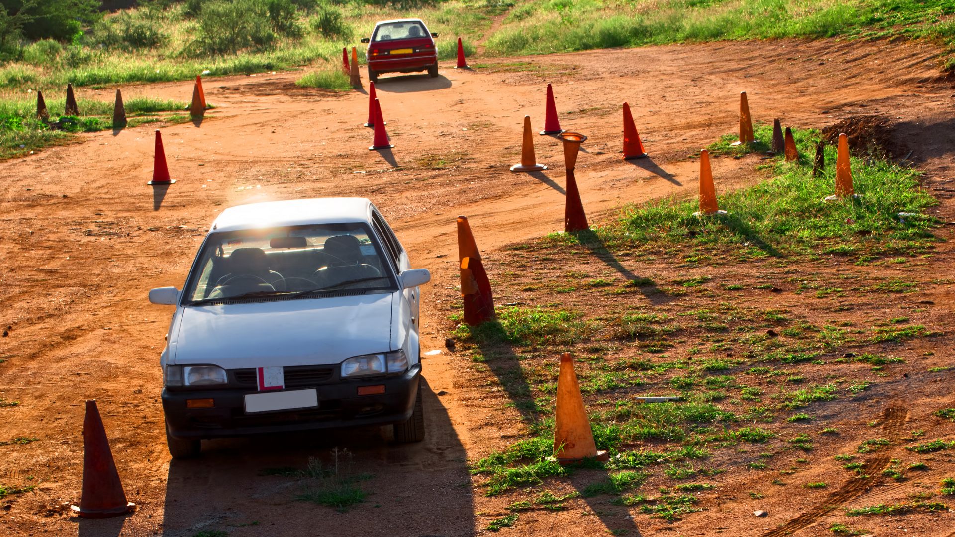 Cars navigating cone-lined dirt road in sunlight.