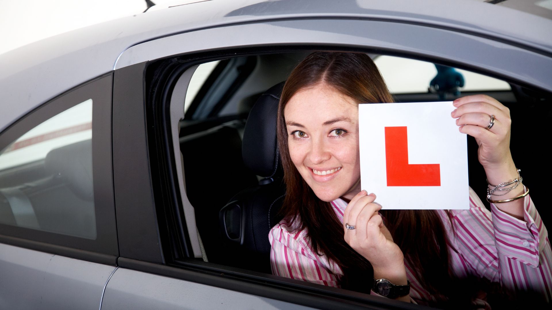 Young woman displaying learner's permit in car.