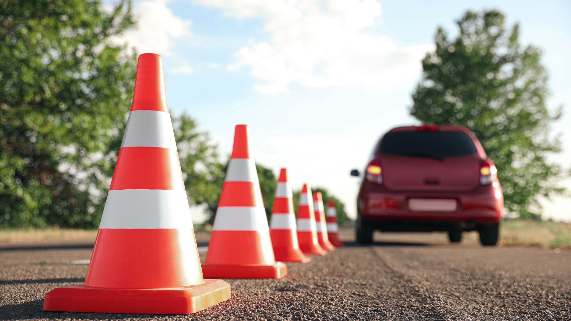 Traffic cones and red car on a road.